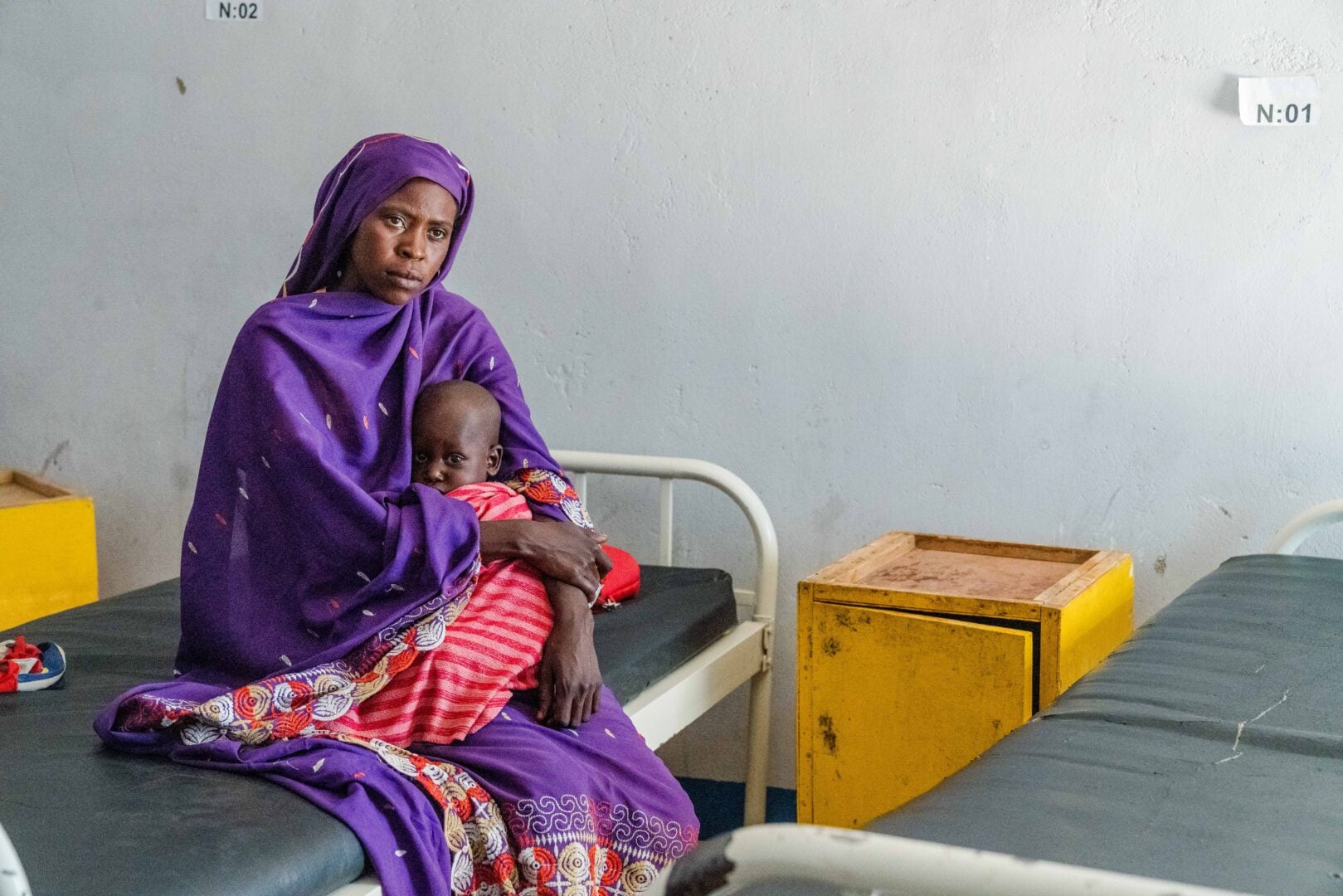 A woman sitting on a hospital bed holds a child in her lap.