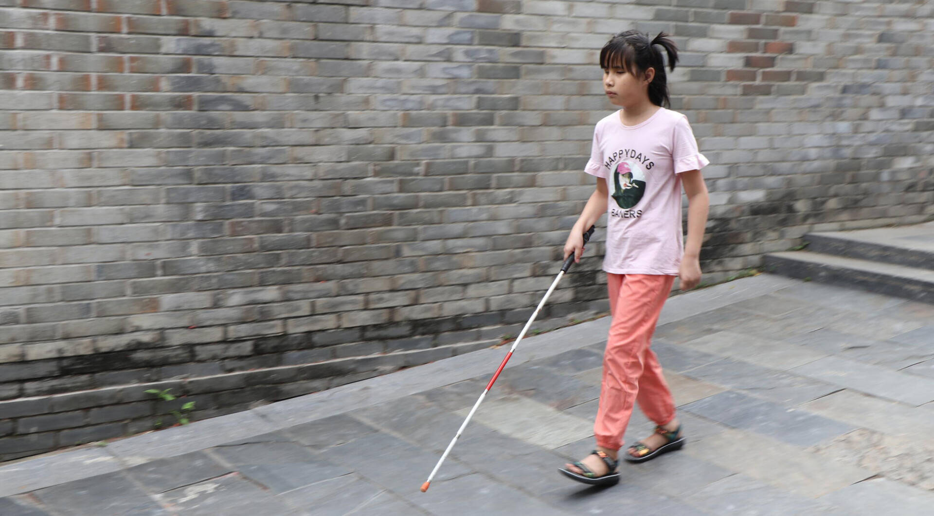 A Chinese girl takes a step with guidance from her walking stick.