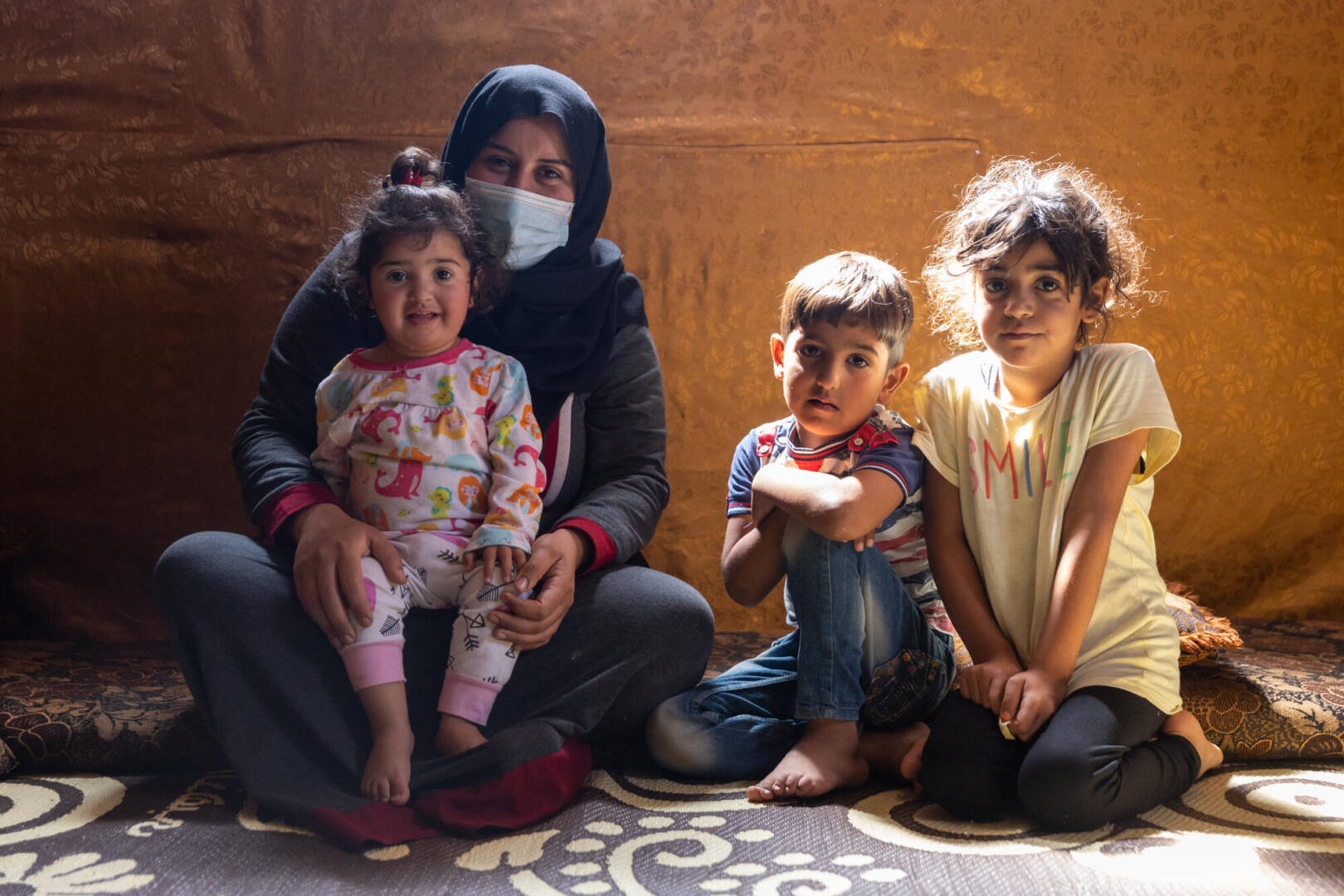 Abir and her three children look toward the camera in an informal settlement in Lebanon